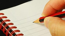Hand taking notes with a pencil on a notebook