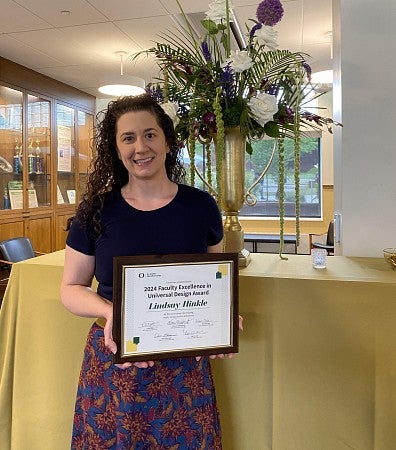 Lindsay Hinkle holding her UDL award certificate in front of a table with flowers